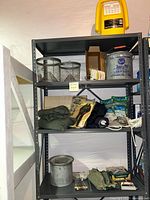 Three-tier metal shelving unit with fishing gear including minnow buckets, fish traps, ropes, rain jackets, and a pump.
