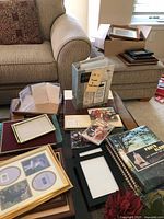 Overview of wood and metal photo frames and photo albums arranged on a coffee table and armrest of sofa.