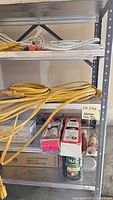 Shelf displaying multiple yellow extension cords coiled and laid out, with white cords on upper shelf and fire extinguishers, and can also visible