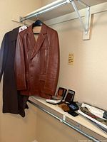 Brown men's leather jacket size 40 hanging on rack with assorted wallets and ties on shelf below, well-lit closet corner.