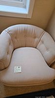 Close up photo of cream colored barrel-back armchair corner showing button tufting on curved back.