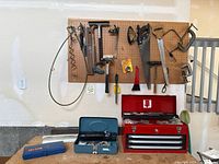 Pegboard with a variety of hand tools hanging, including hammers, clamps, saws, and other tools, plus a blue Cen-Tech socket set and red Sears Craftsman toolbox below.