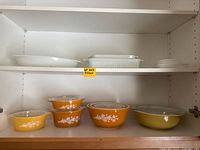 Wide shelf view showing complete lot of yellow Pyrex and white glass baking dishes and bowls.