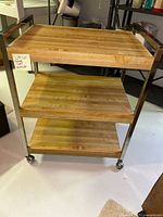 Full view of the wood rolling cart showing three wooden shelves and metal frame with wheels.