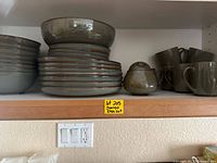 Shelf with stacked Sango stoneware dishes including bowls, cups, creamer or sugar bowl with lid, and stacked plates.