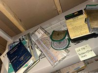 Overview photo of all flight-related items spread on a white surface, showing books, a navigation plotter sealed in plastic, a circular instrument, and other materials.