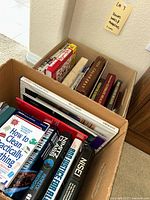 Top view of boxed assortment of books including visible titles 'How to Clean Practically Everything,' 'Nisei,' and 'Madison'