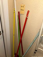 Photo showing multiple colorful broom handles and a mopstick clustered in a pantry corner