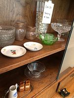 Displaying assorted glassware and decor items on wooden shelves inside a China cabinet.