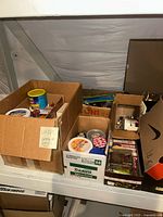 Boxes full of various small hardware and electrical items in cardboard boxes in storage area.