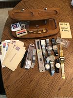 Overview showing eight watches, wooden organizer, postcards, tie clips and stamps on table