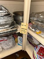 Photo of shelves with stacked aluminum serving pans both square and round, along with paper towels and boxed disposables below.