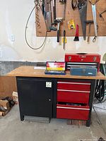 Workstation showing black cabinet door on left and red three drawers on right with items on top and pegboard wall behind.