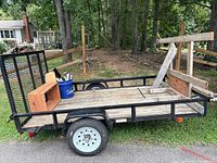Right side view of trailer showing steel frame, wood deck, mesh ramp gate, wood rails, single axle and tire