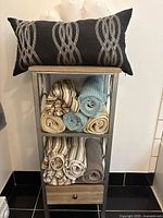 Cabinet with pillow on top and rolled towels on shelves