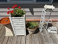 Full lot showing bird bath, tall wood planter with geraniums, round planter with nasturtium, metal plant stand, small terrarium