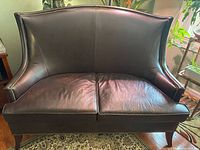 Front view of dark brown leather loveseat, high back, nailhead trim, wood legs