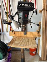 Front view of Delta drill press showing head, handles, wooden table, lamp