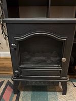 Front view of black metal electric fireplace heater with closed mesh door