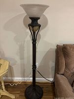 Full view of metal torchiere floor lamp beside couch