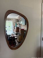 Full view of mirror hanging on wall showing asymmetrical shape and wood frame
