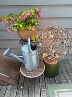 Entire lot showing watering can, table, begonia in terracotta pot, lighted metal sphere on green ceramic planter
