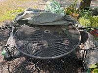 Round wrought iron mesh patio table with chairs folded beneath tarp
