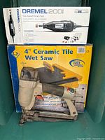 Boxed Dremel 200 rotary tool atop boxed QEP 4" wet saw with Porter Cable nailer in front