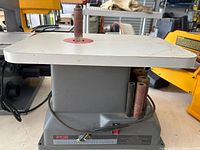 Front view of Ryobi oscillating spindle sander with sanding sleeves and extra spindles stored on side
