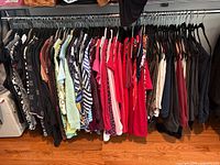 Full rack of assorted women’s clothing—shirts, tops and pants in assorted colours and prints