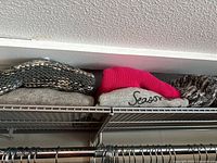 Folded sweaters and pink beanie on upper shelf