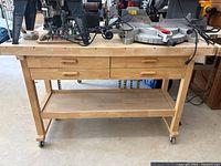 Front view of wood workbench showing drawers, lower shelf, casters, tools on top not included