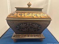 Front view of black and gold painted resin storage box with pineapple finial