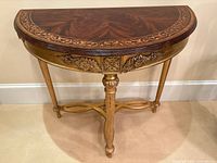 Front angled view of demilune console showing mahogany veneered top, carved gilded apron, fluted legs and X stretcher