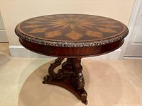 Full view of round pedestal accent table showing marquetry top, gilt apron, and pedestal base