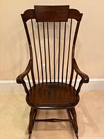 Front view of dark brown Windsor-style rocking chair showing high spindle back, curved arms and sculpted seat