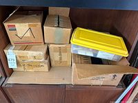 stack of six cardboard boxes and one plastic bin on shelf