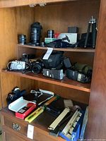 Shelf with multiple cameras, lenses, flashes, binoculars and accessories