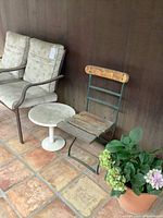 Overall view showing one cushioned patio chair, side table, one folding chair and potted plant