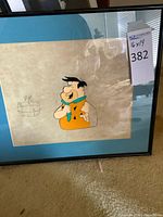 Front view of framed Fred Flintstone production cel showing character art, matting and frame