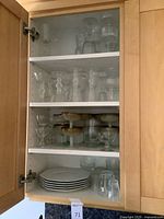 Cabinet with three shelves showing stacked stemware, amber dessert goblets, white plates and tumblers