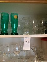 Cabinet shelf with two green pilsner glasses, multiple wine glasses