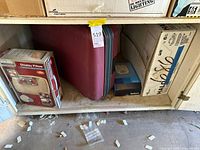 Shelf holding red suitcase, Shiatsu Pillow box, blue-white box, and Hamilton Beach box