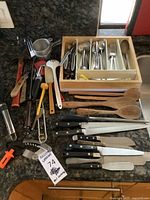 Overall view of flatware, knives, utensils, measuring cup, thermometer, garlic press, corkscrew, hammer