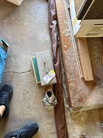 Closed grey tackle box on concrete floor beside packaging and partially visible rod