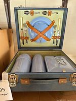 Open picnic hamper showing exterior texture, interior straps, plates, cutlery, thermos bottles and storage box