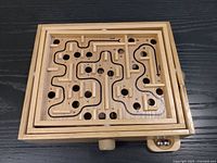 Top view of wooden labyrinth showing track, holes, knobs and a steel ball in storage corner