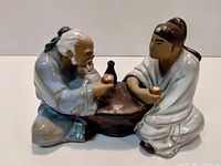 Front view of multicolor ceramic figurine showing two kneeling figures at a table holding cups