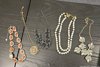 All five necklaces laid out side by side on dark surface