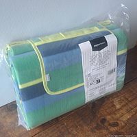 Folded striped picnic blanket in plastic wrap showing carry handle and flap